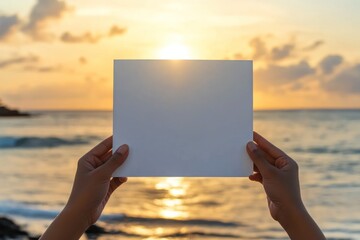 Wall Mural - a person holding a blank sheet of paper against a sunset backdrop by the ocean.