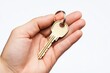© BerkahStock - A hand holding a gold key on a keyring against a plain background.
