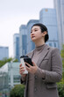 © zhouyilu - Confident Businesswoman in Urban Setting with Smartphone and Coffee