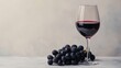 © klss777 - A glass of red wine and plump black grapes against a soft gray background invite indulgence.