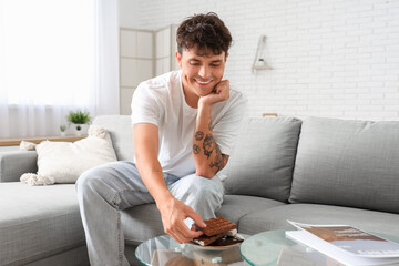 Poster - Handsome young man and plate with sweet chocolate bars on table in living room