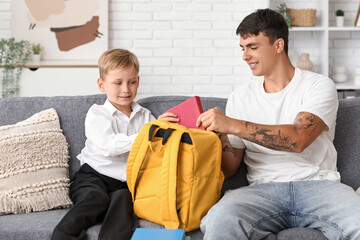 Canvas Print - Father and his little son packing books into backpack at home