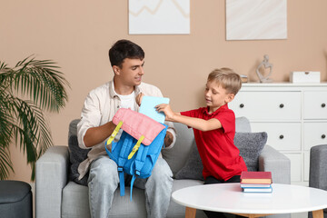 Canvas Print - Father and his little son packing books into backpack at home