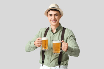 Young man in traditional German clothes with mugs of beer on white background. Octoberfest concept