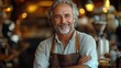 © Emile - A portrait of a mature man or waiter with an apron in a coffee shop represents customer service, employment, small business, a happy barista, hospitality, and confidence.