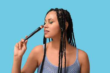 Wall Mural - Young African-American woman with braids and beautiful makeup holding brush on blue background