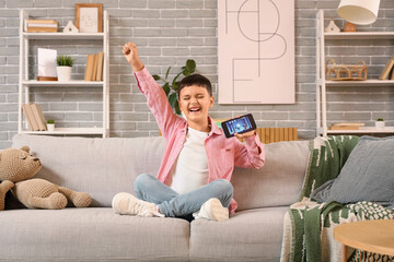 Canvas Print - Cute happy little boy with mobile phone playing video games on sofa at home