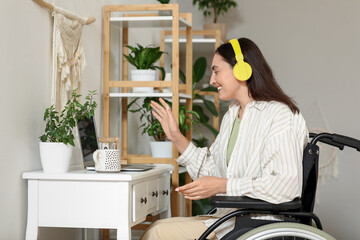 Wall Mural - Young woman in wheelchair with headphones and laptop video chatting at home