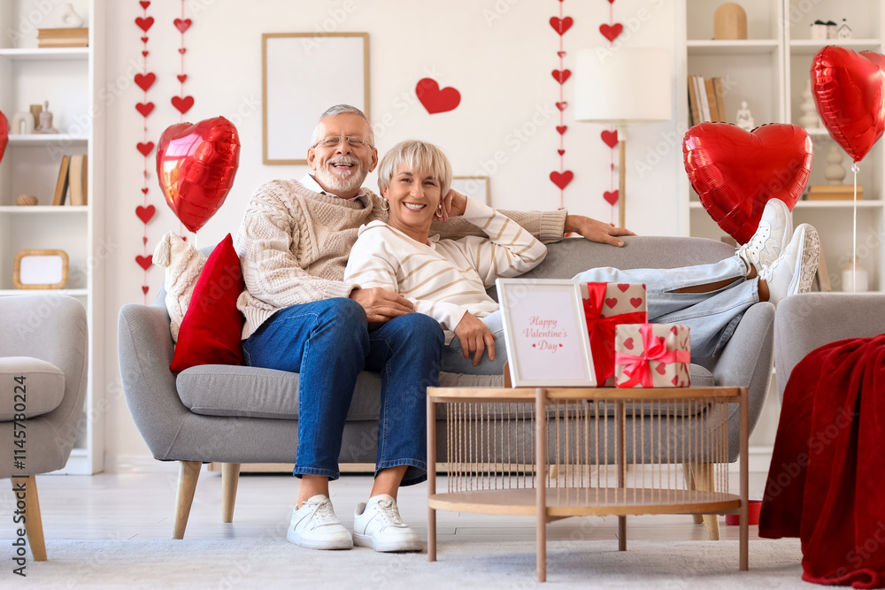 Happy mature couple with gift boxes sitting on sofa at home. Valentine's Day celebration