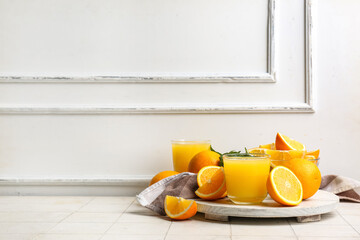 Wall Mural - Wooden board with glasses of tasty juice, oranges and mint leaves on white tile table