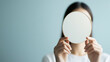 © fotofabrika - Person holding a round mirror in front of their face against a light blue background