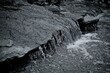 © ChaoticMind - A black and white image of a gentle stream cascading over a rocky ledge, depicting the simple yet captivating motion of water in a minimalist natural setting.