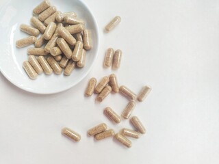 Supplement capsule pills in a small white plate on a white background.