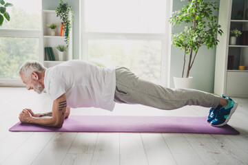 Wall Mural - Elderly man practicing a plank exercise on a yoga mat indoors, maintaining fit body with healthy lifestyle