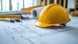 © THIPPAYASAN 8995 - Yellow construction helmet placed on architectural blueprints with tools and rolls of paper in the background, symbolizing building and design projects in progress