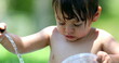 © Marco - Toddler boy playing with water hose outdoors during summer day inside bucket