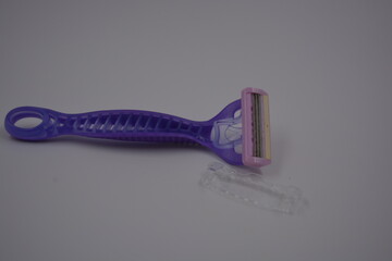 Objects for female beauty, things for the omission of everyday life. A purple, sporty plastic shaving machine is located on a white plastic background.