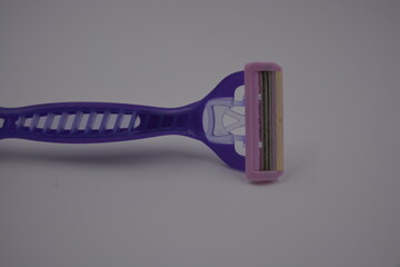 Objects for female beauty, things for the omission of everyday life. A purple, sporty plastic shaving machine is located on a white plastic background.