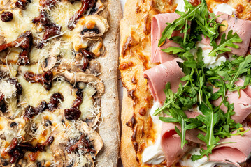 Wall Mural - A delicious view of two types of pizza: one topped with mushrooms and sun-dried tomatoes, and the other with ham, arugula, and creamy sauce. Perfect for food lovers and culinary presentations.