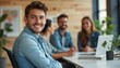 © kotlyarn - A cheerful young man with light brown hair smiles warmly at the camera, surrounded by colleagues in a bright, contemporary office. The atmosphere is vibrant and collaborative, showcasing teamwork and