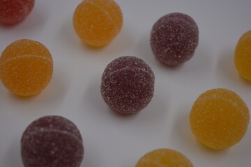 Original jelly Finnish candies in the form of round balls covered with white sugar. Yellow, orange, cherry, red gummy candies are located on a white plastic background.