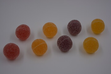 Original jelly Finnish candies in the form of round balls covered with white sugar. Yellow, orange, cherry, red gummy candies are located on a white plastic background.