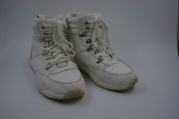 Things, household items, white shoes with an interesting sole, white laces. An unwashed, old, worn pair of women's shoes with metal rivets and a worn leather surface are located on a white plastic.