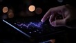 © VANATSANUN - A hand interacting with a tablet displaying digital data and graphs in a dark setting.