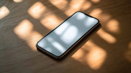 Wall Mural - Smartphone with blank screen on wooden table in sunlight.