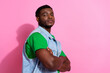 © deagreez - Stylish young man standing confidently against a vibrant pink background, wearing a denim waistcoat over a green shirt.