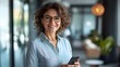© Ben Kuang - Smiling middle-aged woman with curly hair and glasses, holding a smartphone in a modern setting.