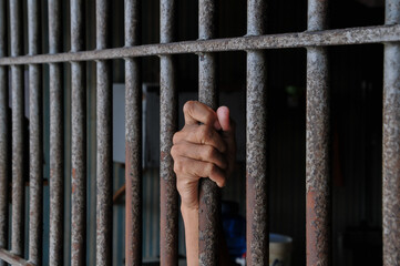 prisoner's hands behind bars with black background