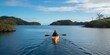 © Metthaisonk - Person kayaking on serene blue water with lush green islands in the distance under a cloudy sky.