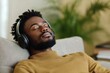 © DigitalMagicVisions - Calm and Relaxed Man Enjoying Soothing Music with Headphones While Sitting Comfortably on a Sofa Surrounded by Nature-Inspired Decor