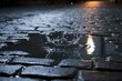 © Qalandar - A raindrops impact creates a crown splash in a puddle on a dark, wet cobblestone street. The blurry background suggests falling rain. Light reflects on the water.