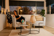 © Austockphoto - Woman in black dress looking out window from cosy armchair in warmly lit room