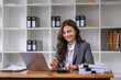 © wichayada - Confident Business Woman Working at Office Desk with Laptop and Documents in Modern Workspace