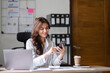 © wichayada - Young Businesswoman Analyzing Documents in Modern Office Setting with Laptop and Smartphone