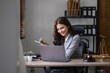 © wichayada - Young Businesswoman Analyzing Documents at Desk in Modern Office Setting with Laptop and Professional Attire