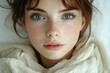 © prophoto - Close-up portrait of a young woman with freckles and green eyes, wearing a cream-colored scarf.