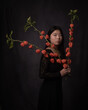 © Milou Dirks - classic painterly dark renaissance portrait of a young asian woman in black dress holding orange lantern flowers