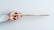 © kinara art design - Close-up of a hand holding a long, thin, light brown wooden stick against a white background.