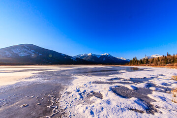 Wall Mural - A frozen lake with snow on the mountains in the background