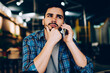 © BullRun - Contemplative hipster guy thinking aver plans for meeting while talking on telephone with friend in cafe, pensive young man waiting for connection with customer support line on mobile phone
