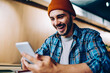 © BullRun - Overjoyed male in hat surprised with victory in online competition in social networks getting notification on cellular, amazed hipster guy happy about winning discount for online courses studying