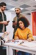 © BullRun - Portrait of african american female designer smiling at camera while working together with colleagues on new building project in office studio.Male and female students collaborating in university
