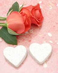 Wall Mural - Two white heart-shaped items beside red roses on a pink background.