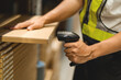 © KANGWANS - A person is using a barcode scanner in a warehouse. The person is wearing a yellow vest and black pants