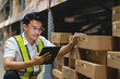 © KANGWANS - A man in a yellow vest is looking at a tablet while standing in a warehouse. He is wearing glasses and he is focused on the tablet
