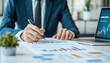 © Leninya - businessman analyzing financial documents and charts in office setting. He is focused on data, showcasing professional environment with laptop and plant nearby